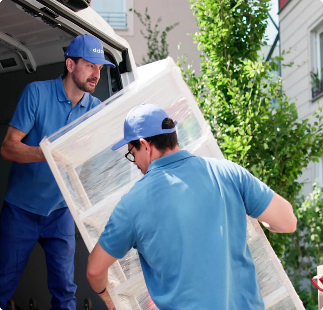 Two professional courier drivers carefully carrying large furniture item into van
